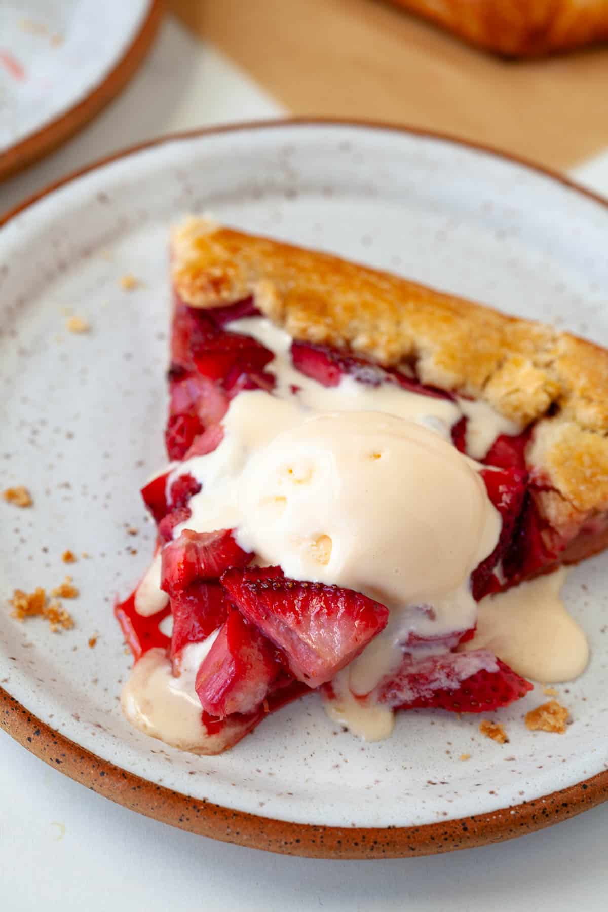 slice of strawberry rhubarb galette topped with vanilla ice cream on white speckled plate