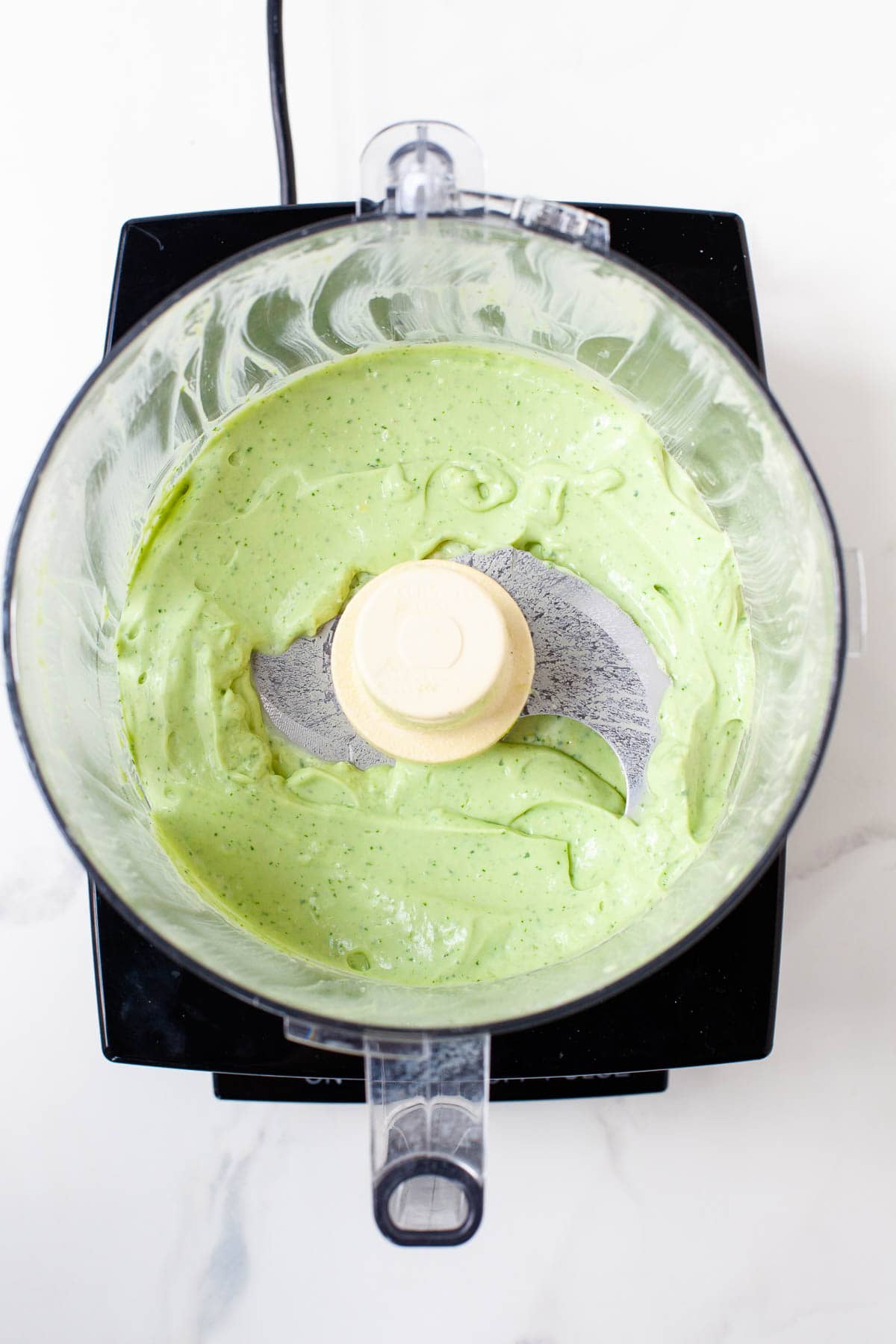 avocado lime crema in food processor after blending on white marble surface