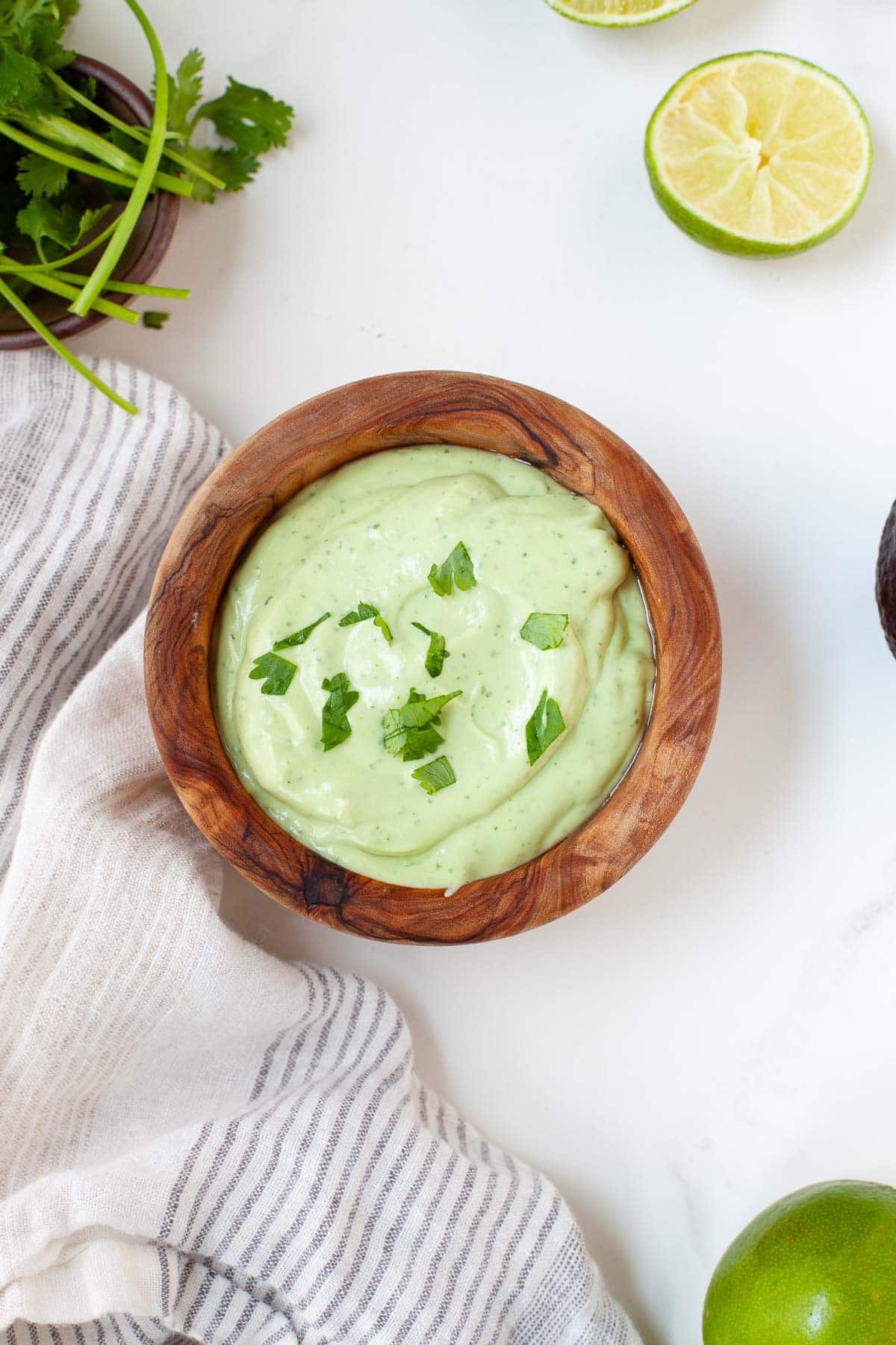 Avocado lime crema garnished with fresh chopped parsley in small wooden bowl